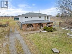 View of front facade with brick siding, a front lawn, a view of rural / pastoral area, roof with shingles, and driveway