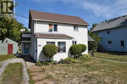 View of front of house with a front yard, roof with shingles, and a storage shed