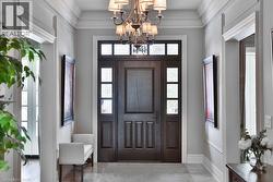 Entryway featuring a paneled wood door with frosted glass sidelights and transom, chandelier lighting, crown molding, and light-toned flooring