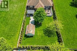Spacious rear yard featuring extensive green lawn, perimeter fencing with mature shrubs, a detached storage shed, a stone patio, and an elevated wood deck