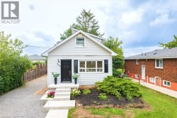 White siding exterior with black shutters, concrete front steps, landscaped front garden beds, a gravel driveway, and a wooden fence