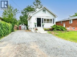 Gravel driveway leading to a white exterior home with black shutters, a step up entry, and a dormer window