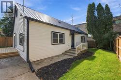 White siding exterior with black trim windows, a black metal roof, a wooden deck, a concrete patio, and a grassy lawn