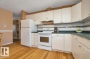 Kitchen featuring wood-finish flooring, white cabinetry, a white tile backsplash with decorative accent, and dark countertops