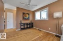 Living area featuring warm-toned walls, wood-finish flooring, a ceiling fan, and a large window