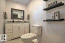 Bathroom featuring a white vanity with panel door and drawer fronts, a gray countertop, a framed wall mirror, a commode, and dark floating wall shelves