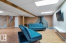 Finished lower level featuring wood-finish flooring, drop ceiling with integrated lighting, wood-clad support beams, and a tile-surrounded wood-burning stove