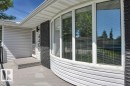 Curved bay window featuring horizontal blinds, black brick accent, light gray siding, and a front entry with an overhead fixture