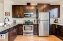 Kitchen featuring wood-finish flooring, dark wood cabinetry, light-toned countertops, a stainless steel refrigerator, and a stainless steel oven/range