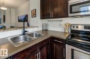 Modern kitchen featuring a double stainless steel sink with a matte black faucet, dark wood-finish cabinetry, light-toned countertops, a stainless steel microwave, and a stainless steel and black range