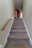 Carpeted staircase with a natural wood handrail, leading to an upper level with light-toned walls and ceiling