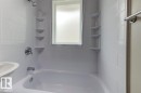 White subway tile surround with integrated corner shelving, white bathtub, chrome shower fixtures, and frosted window