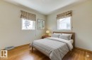 Bedroom featuring two windows with striped Roman shades, wood-finish flooring, and light-toned walls