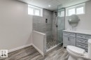Contemporary bathroom featuring a glass-enclosed shower with subway tile surround and pebble flooring, a light gray vanity with a white countertop and oval mirror, and wood-finish flooring