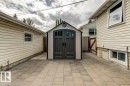 Arched-door storage shed with decorative windows positioned on a stone paver patio