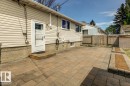 Rear exterior featuring cream-colored siding, a white storm door, and a multi-toned paver patio