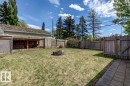 Spacious backyard featuring a block paver fire pit, wood fencing, chain link fencing, a covered storage area, and a paver stone patio