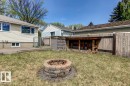 Expansive backyard featuring a stone-paver fire pit, a concrete patio, a wood fence, and a wood storage structure