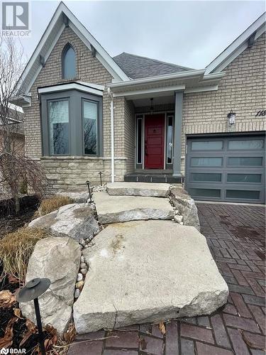 View of front of home with a garage, brick siding, stone siding, roof with shingles, and decorative driveway