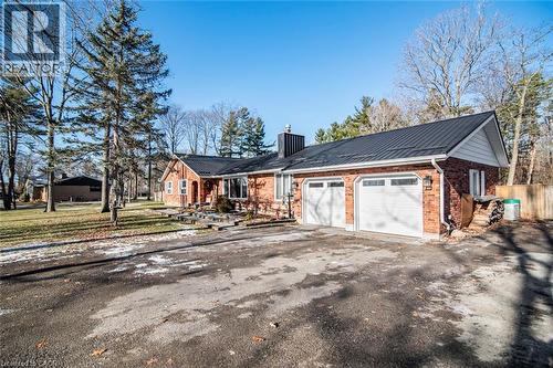 View of front of property with a metal roof, a chimney, brick siding, driveway, and an attached garage