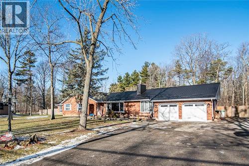 View of front facade with brick siding, driveway, a chimney, and a garage