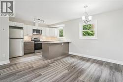 Kitchen with stainless steel appliances, decorative light fixtures, white cabinetry, a peninsula, and light wood-style floors