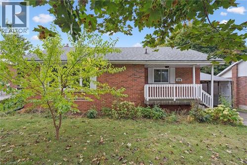 View of front of house with covered porch, a front yard, a shingled roof, and brick siding
