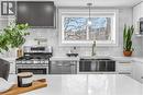 Kitchen with stainless steel appliances, light stone countertops, ventilation hood, decorative light fixtures, and white cabinets