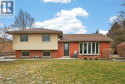 Rear view of property featuring brick siding, a lawn, a patio, and a shingled roof