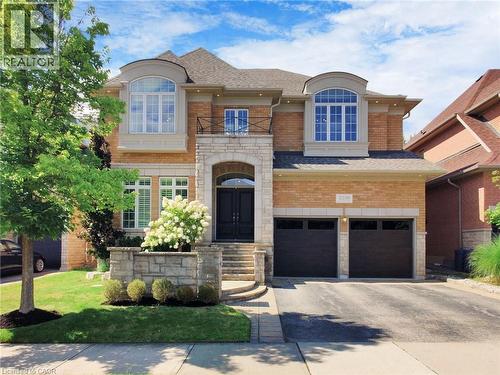 View of front of property featuring stone siding, a balcony, driveway, brick siding, and an attached garage