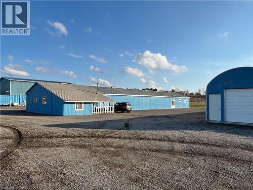 The property features multiple blue-painted structures, including a building with a gray sloped roof and white railing, and a Quonset hut style building with a white garage door