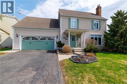Charming two-story property featuring a front porch entry, a two-car garage with decorative hardware, and a well-maintained lawn with mature trees and shrubs