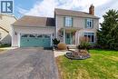 Charming two-story property featuring a front porch entry, a two-car garage with decorative hardware, and a well-maintained lawn with mature trees and shrubs