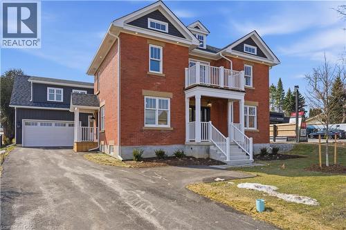 The property features a red brick exterior with white trim, a double garage with a white door, and a front entrance with a covered porch and balcony