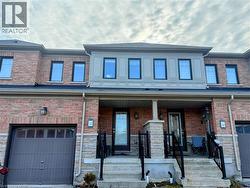 Brick and stone facade townhome featuring a front porch, individual garage, black-framed windows, and exterior lighting fixtures
