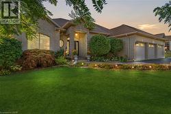 Brick exterior with a three-car garage, established landscaping, and accent lighting