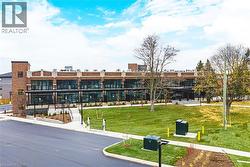 Brick and glass building featuring multiple levels of balconies, a prominent brick tower, and a well-maintained lawn area with mature trees and paved walkways