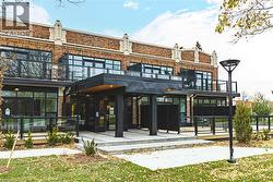 Brick facade building featuring a grand entrance with a dark metal canopy, large windows, glass panel balconies, and a concrete pathway