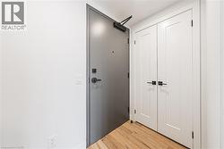 Entryway featuring a solid gray door with black hardware, white double doors with black hardware, white walls, and wood-finish flooring