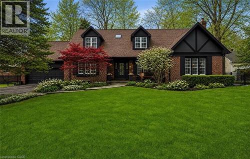 Brick facade residence featuring dark trim, a prominent front lawn, a paved driveway, and mature landscaping