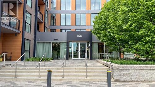 Contemporary building facade featuring a prominent main entrance with large glass doors, an overhead number sign, and a stone staircase with metal railings