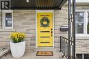 Stone veneer exterior with a vibrant yellow entry door, modern black railings, white window frames, and a recessed ceiling light