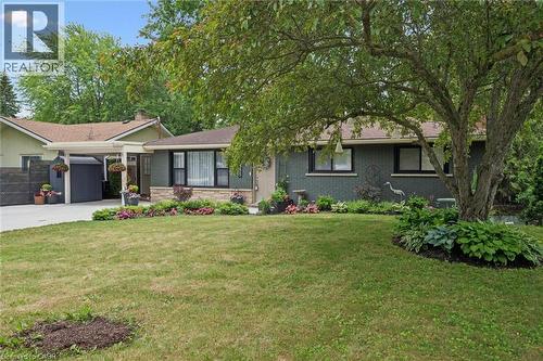 Front exterior featuring a brick facade with stone detailing, a covered carport, mature trees, manicured landscaping, and a paved driveway