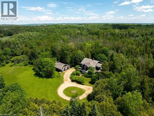 Expansive property featuring a main residence with a gabled roof and a secondary structure, both nestled within a heavily wooded landscape