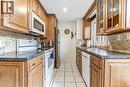 Galley kitchen featuring maple cabinetry, tile flooring, stone-look countertops, and a full suite of appliances including a stainless steel refrigerator and built-in microwave