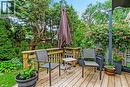Wood-finish deck with natural wood railings, surrounded by mature trees, varied plantings, and a climbing floral trellis