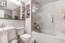 Bathroom featuring a pedestal sink with brushed nickel faucet, tiled walls, built-in recessed shelving, a white toilet, and a soaker tub with clear glass enclosure