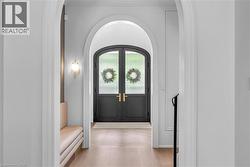 Arched entryway featuring double doors with glass panels, light wood-finish flooring, and a built-in wall sconce