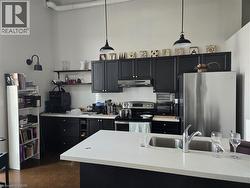 Kitchen featuring dark cabinets, stainless steel appliances, decorative backsplash, decorative light fixtures, and a high ceiling