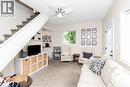 Carpeted living area featuring a ceiling fan, a window with exterior views, a white door with glass panels, and a staircase with a white railing